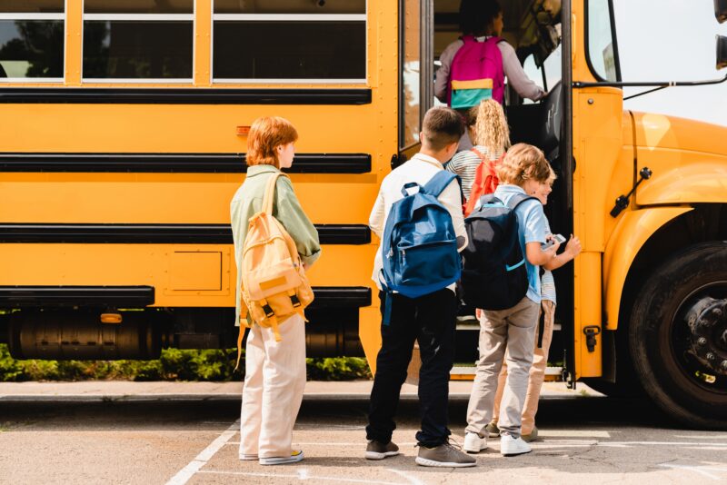 Children lined up to board a yellow school bus.